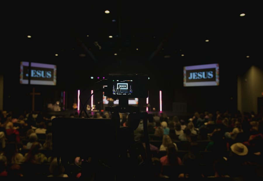 Large room with an audience facing wall-mounted projection screens
